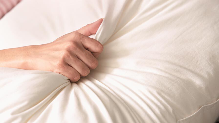 Detalhe de mão a apertar lençol, simbolizando intimidade e orgasmo feminino 